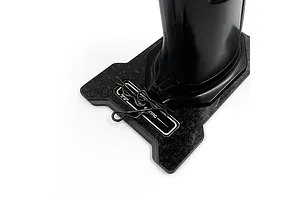 A close-up of a carbon fibre base plate for an RC transmitter, featuring a Yeah Racing logo and two metal body clips resting on the surface.