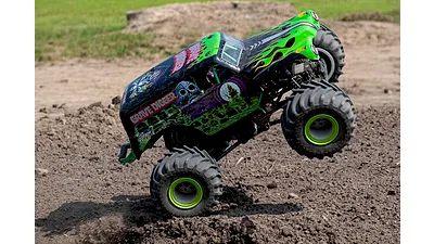 A Grave Digger RC monster truck performing a wheelie on a dirt track outdoors.