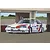 An illustration of a white 1986 Nissan Skyline RS Turbo race car with red and blue racing stripes and the number 23 parked in a pit garage.