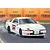 An illustration of a white 1985 Toyota Supra drifting on a racetrack with Tsukuba branding in the background.