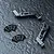 Two black anodized aluminium bulkhead parts for an RC car, accompanied by eight small black countersunk screws, arranged on a dark textured surface.