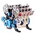A detailed metal model of a V8 engine with gold, blue, and silver components, featuring visible timing chains, pulleys, and exhaust headers.