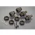 A set of gun metal coloured aluminium RC wheel hubs, locking nuts, pins, and small screws arranged on a grey reflective surface.