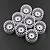 A set of eight white plastic RC car rims with a multi-spoke design arranged on a dark textured surface.