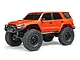 An orange Axial SCX24 Toyota 4Runner RC rock crawler viewed from a front three-quarter angle on a white background.