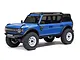 Blue Ford Bronco RC rock crawler studio product shot against a clean white background, showcasing its black roof rack, white wheels, and aggressive tread tires.