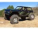A black Axial Wraith 1.9 RC rock crawler driving on a dirt trail under a clear blue sky.