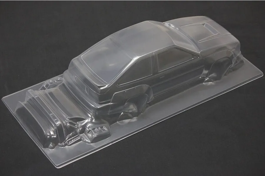 An unpainted, clear polycarbonate 1/10 scale RC car body shell of a Toyota AE86 Trueno N2, viewed from a high angle against a black background.