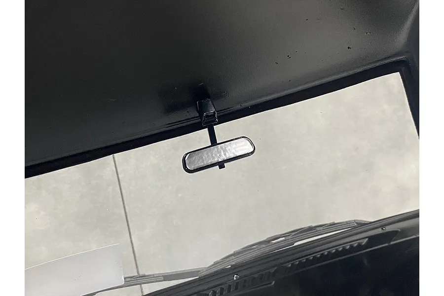 A close-up view of a small black rearview mirror mounted to the interior roof of a scale RC car body.