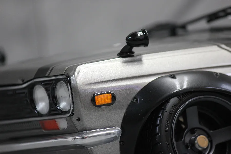 Close-up of a silver RC car body featuring a black fender-mounted side mirror and black wheel arch flares.