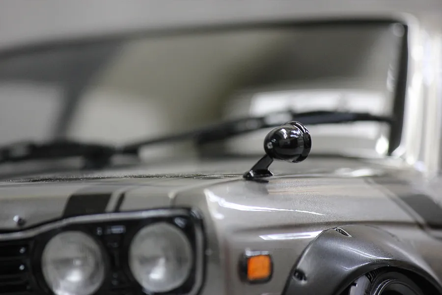 A close-up view of a black fender-mounted side mirror installed on a silver 1/10 scale RC car body.