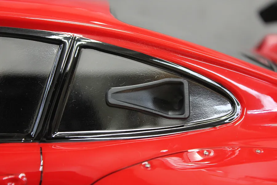 A black NACA duct accessory installed on the side window of a red 1/10 scale RC car body.