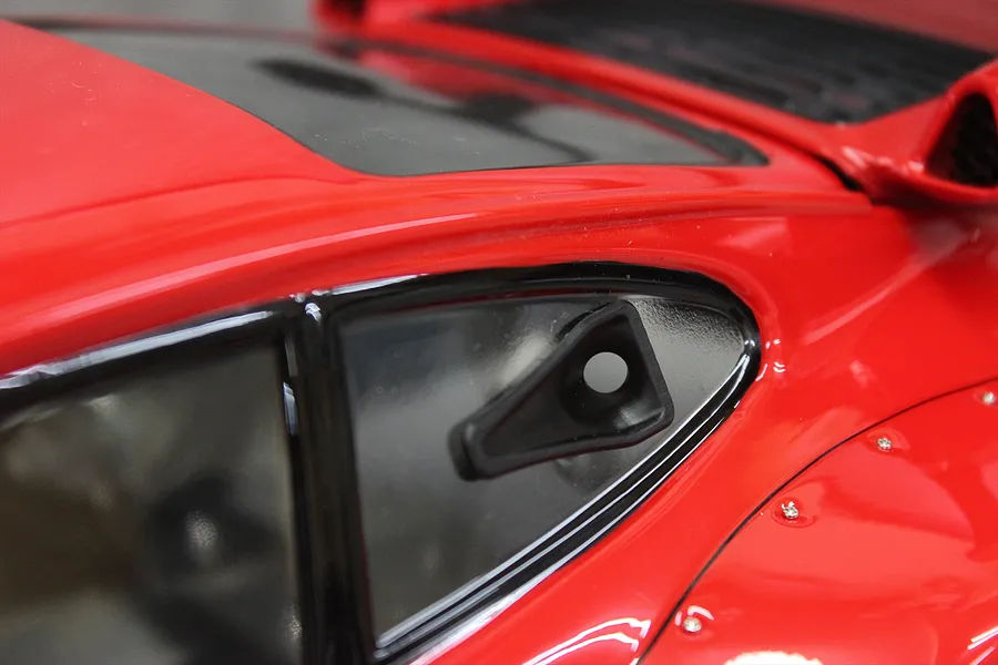 A close-up of a black NACA duct accessory installed on the side window of a red 1/10 scale RC car body.