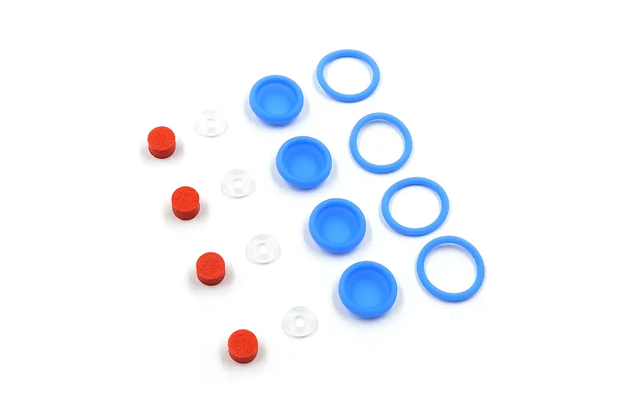 A set of RC shock absorber components including blue silicone membranes, blue O-rings, clear O-rings, and small red foam cylinders on a white background.