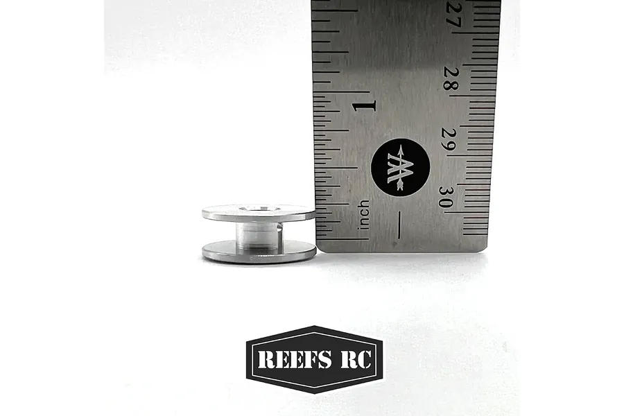 A silver aluminium winch spool for RC vehicles placed next to a metal ruler for scale, with the Reefs RC logo below.