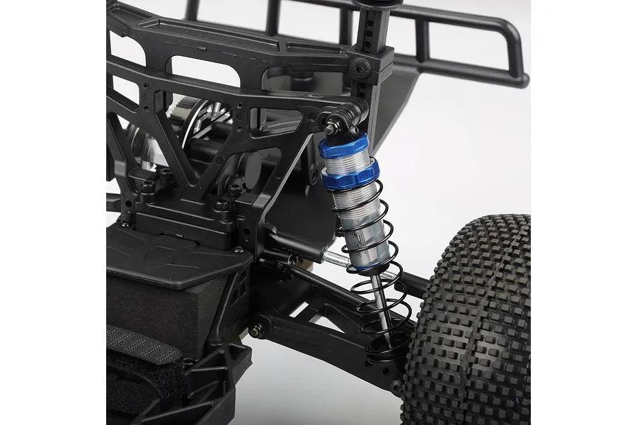 A close-up view of a Pro-Line Pro-Spec shock absorber installed on the rear suspension of an RC vehicle, featuring a blue anodized cap and silver body.