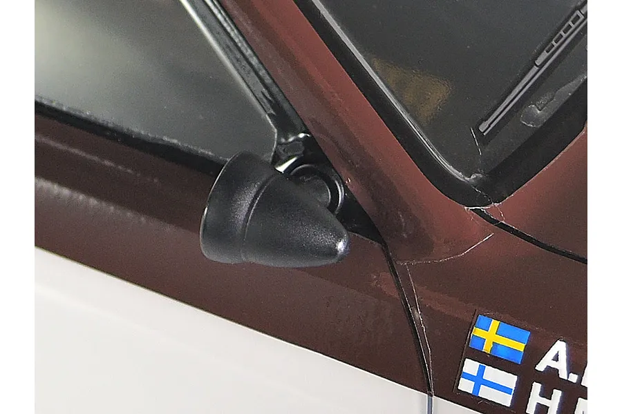 Close-up of a black plastic side mirror mounted on the brown and white painted body of a Tamiya Audi Quattro A2 RC car.