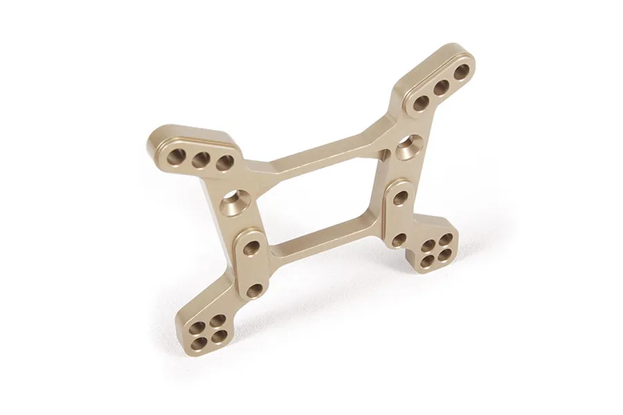 A gold-anodized aluminium RC shock tower with multiple mounting holes, shown from a high-angle perspective against a white background.