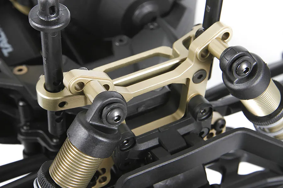 Close-up of an Axial aluminium front shock tower installed on an RC vehicle chassis, featuring a gold-anodized finish and black shock absorbers.