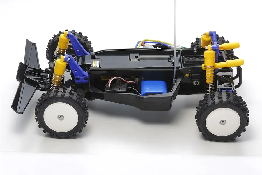 Side view of the Tamiya The Bigwig 2017 RC buggy chassis showing black frame, yellow coil-over shocks, white wheels, and off-road tires.