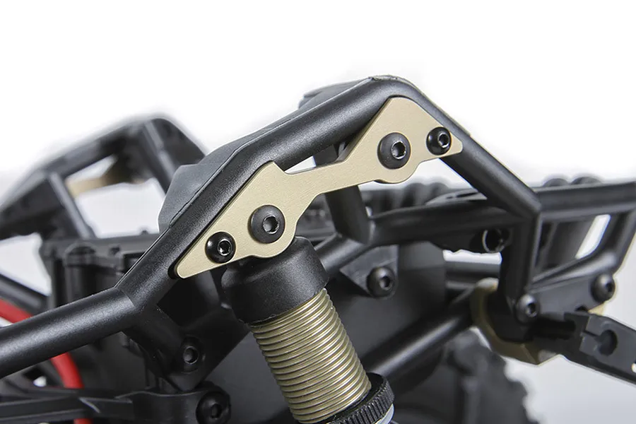 Close-up of gold-coloured aluminium shock mount plates installed on a black RC vehicle chassis frame.