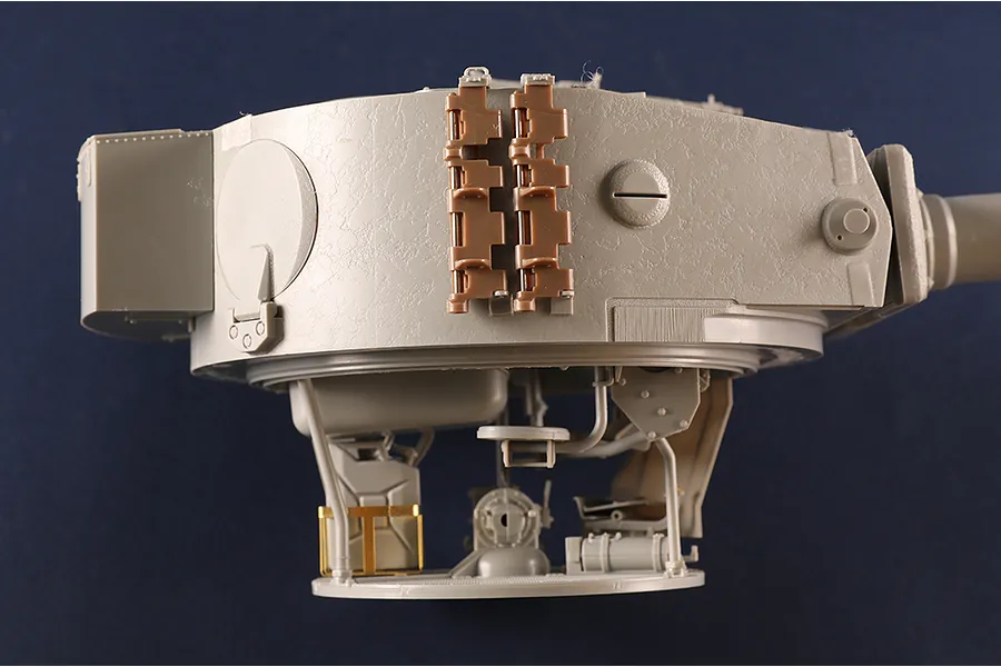 A side view of an unpainted plastic model tank turret showing interior details and exterior track links.