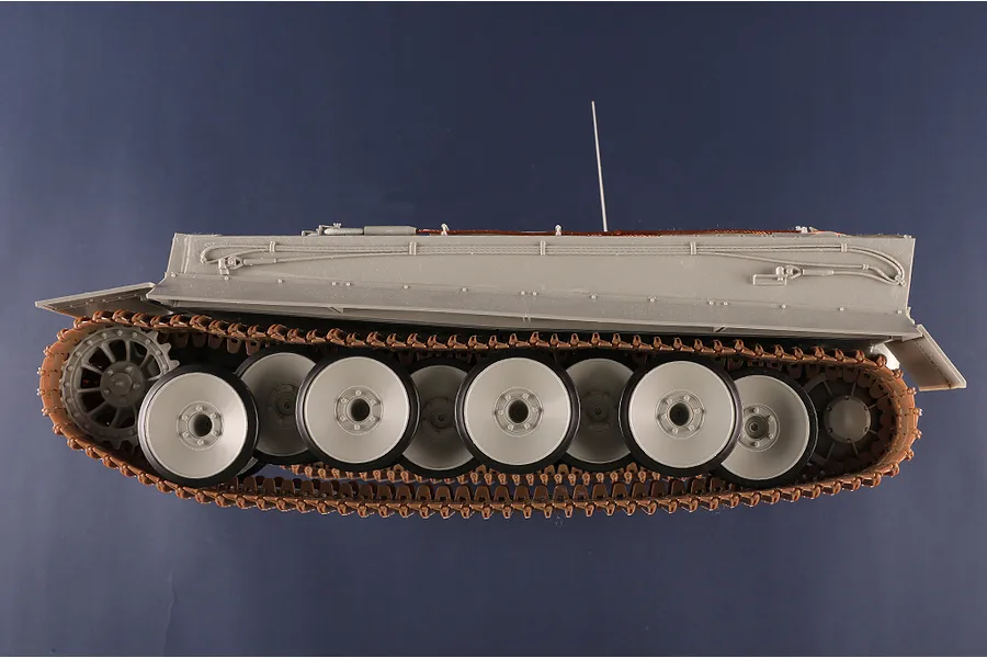Side view of an unpainted 1/16 scale plastic model Tiger I tank showing the hull, road wheels, and tracks against a dark blue background.