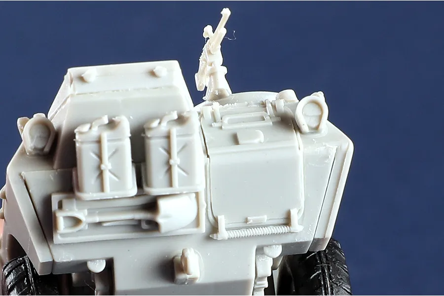 Close-up of an unpainted grey plastic model of an M706 Commando armoured car showing the rear deck with jerry cans, a shovel, and a mounted machine gun.