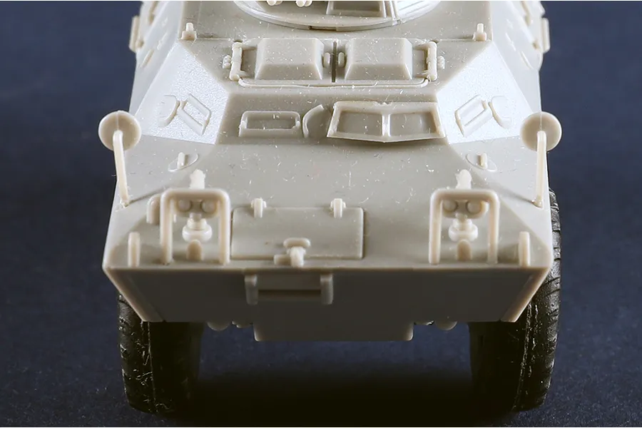 Front view of an unpainted grey plastic model of an M706 Commando armoured car against a dark background.