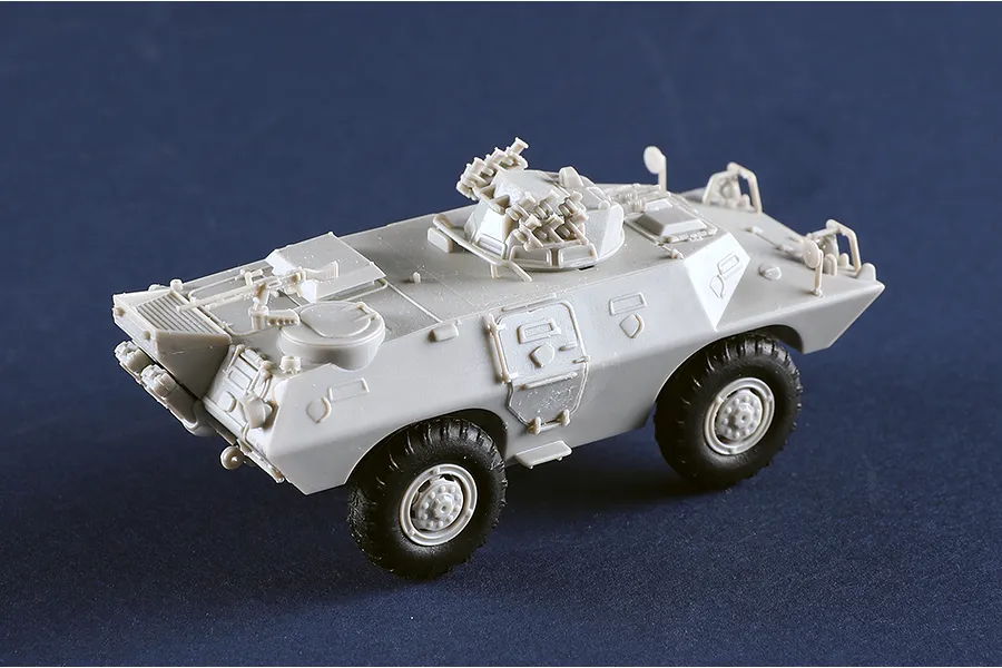 An assembled, unpainted grey plastic model of an M706 Commando armoured car on a dark blue background.