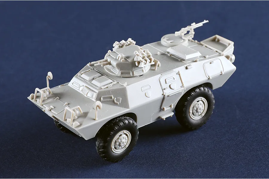 A 1/72 scale plastic model of an M706 Commando armoured car, unpainted in light grey plastic with black wheels, shown from a high-angle perspective.