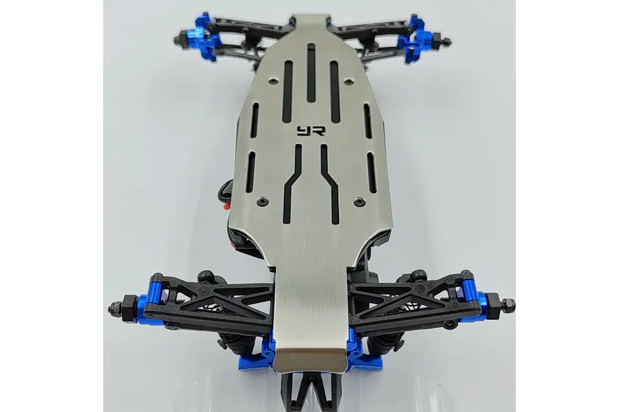 A Yeah Racing stainless steel chassis skid plate installed on the underside of an RC car chassis with blue aluminum components.