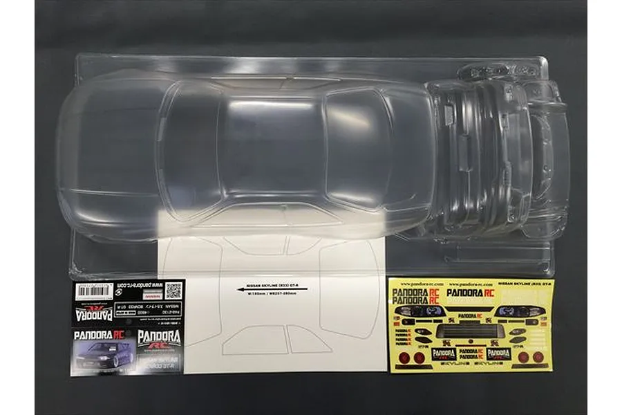 Top-down view of an unpainted clear polycarbonate RC car body shell for a Nissan Skyline R33 GT-R, including decal sheets and window masks.