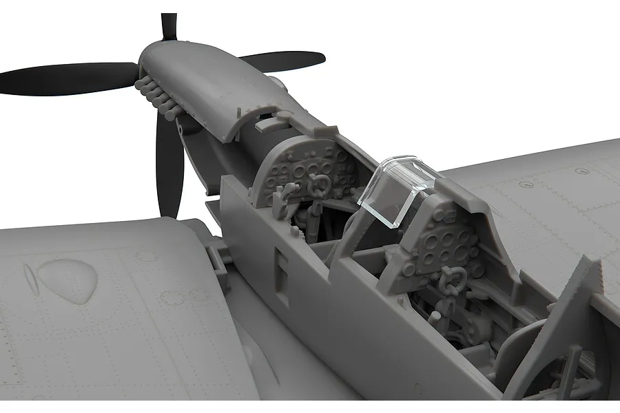 Close-up of an unpainted plastic model Spitfire cockpit showing detailed instrument panels and dual seating.