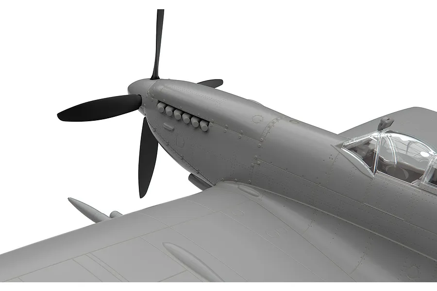 Close-up of an unpainted plastic model Spitfire aircraft showing the nose, propeller, and cockpit area against a white background.