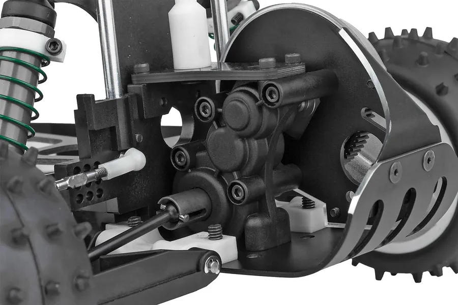 Close-up of the rear suspension and gearbox assembly of a Team Associated RC10 buggy, showing black plastic parts, metal screws, and green coil springs.