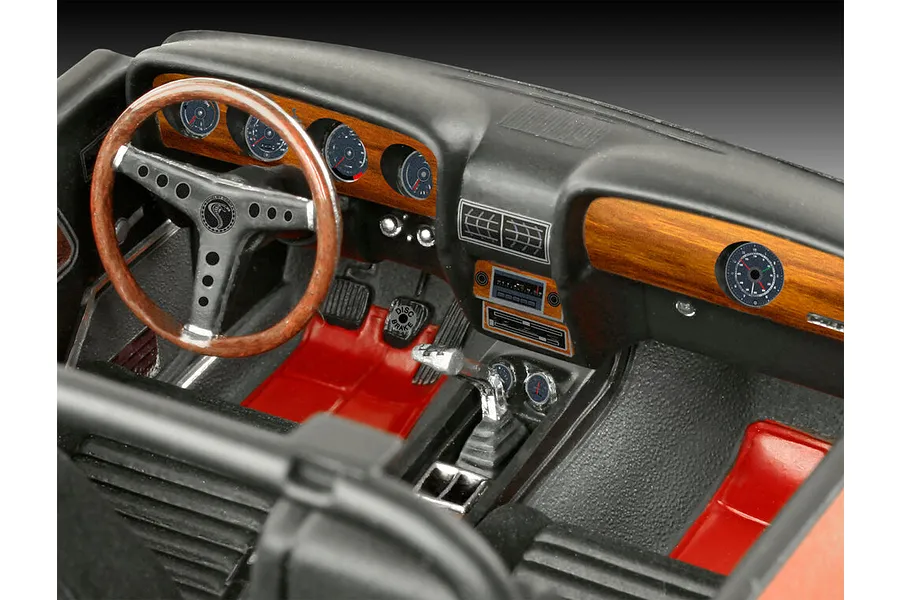 Close-up of the detailed interior of a 1/24 scale 1970 Shelby Mustang GT500 model car, showing the dashboard, steering wheel, and red floor.