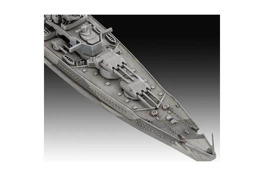 Close-up of the bow section of an unpainted grey plastic model battleship, showing gun turrets and deck details.