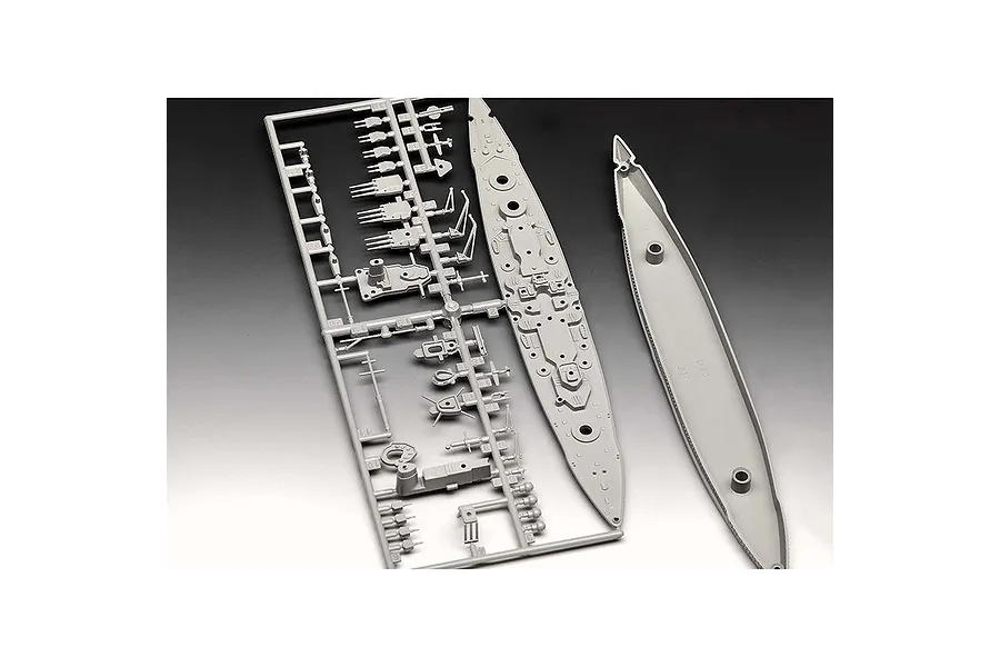 Grey plastic model kit parts for a battleship, including a sprue frame with turrets and the ship deck and hull pieces.