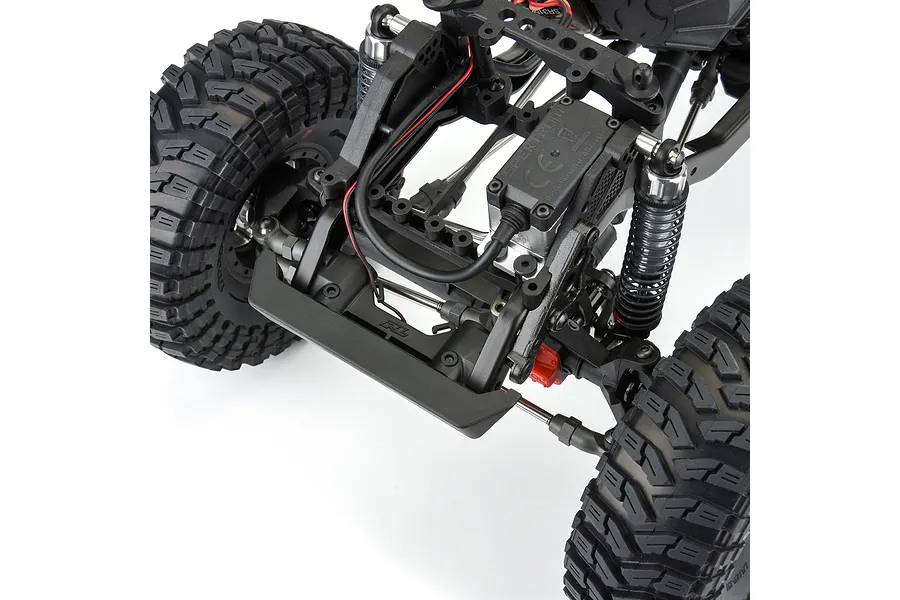 Close-up of a Pro-Line crawler bumper installed on the front of an RC chassis with large off-road tires and suspension components.