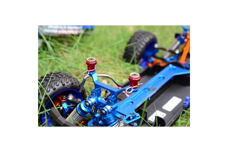 Close-up of blue aluminium magnetic body posts installed on an RC car chassis, sitting on green grass.
