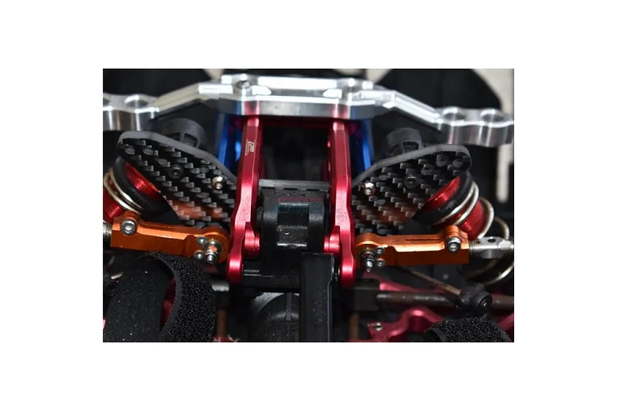 Close-up view of a carbon fibre rear shock tower installed on an RC car chassis with red and orange metal components.