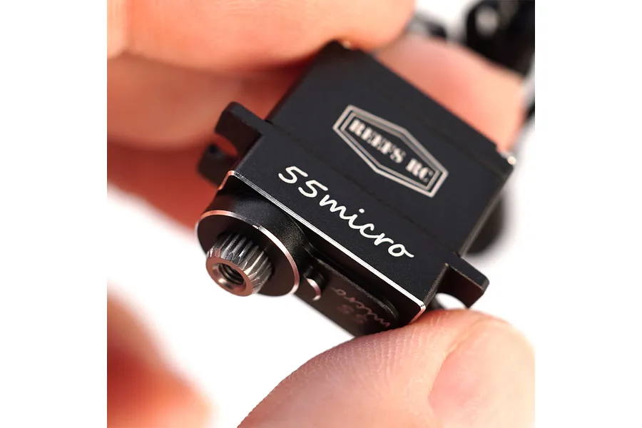 Close-up of a black Reefs RC 55Micro sub-micro servo being held between fingers, showing the metal output gear and branding.