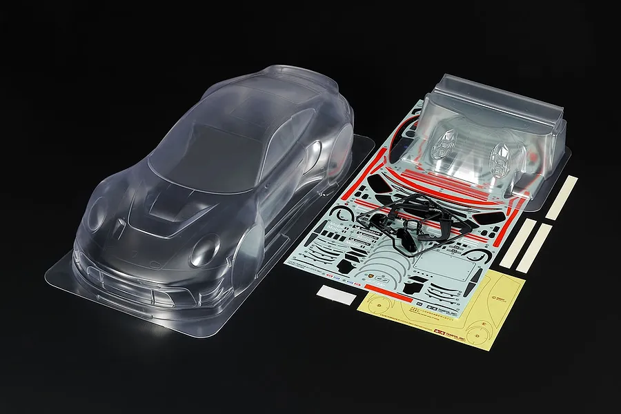 Tamiya 1/10 scale clear polycarbonate Porsche 911 GT3 R 992 RC car body shell with included decal sheet, rear wing, and plastic parts.