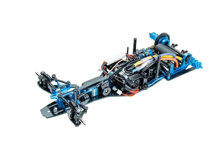A high-angle studio shot of a Tamiya TRF104 RC Formula 1 chassis, showing the carbon fiber frame, blue anodized aluminum parts, and installed electronics.