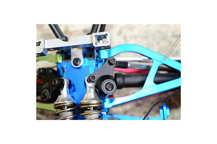 Close-up of blue aluminium rocker arms installed on an RC car chassis with shock absorbers and metal linkages.