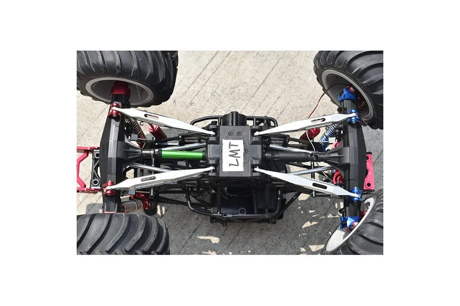 Bottom view of an RC monster truck chassis featuring silver GPM lower link bars installed on the suspension system.