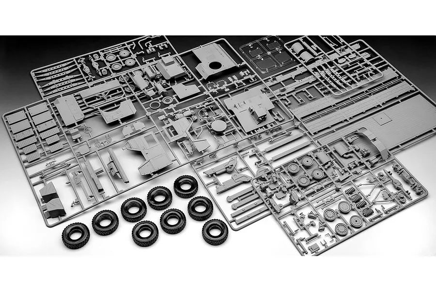 Multiple grey plastic model kit sprues and eight black rubber tires for a 1/35 scale military truck model.