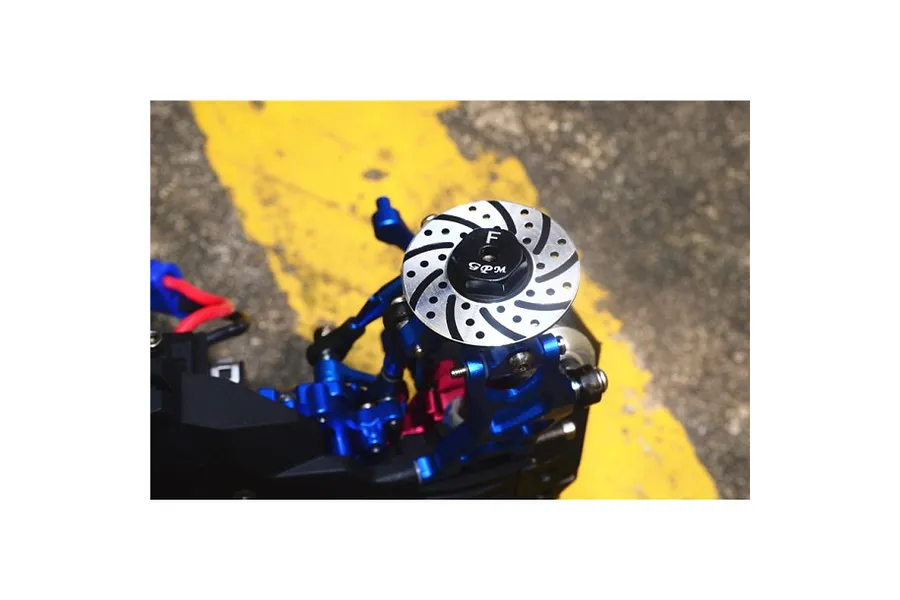 A GPM Racing blue aluminium wheel hex with a decorative brake disc installed on an RC car suspension assembly.
