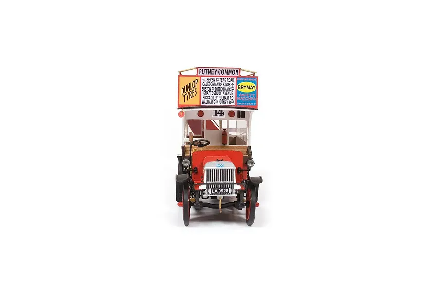 Front view of a finished 1/24 scale OcCre AEC B-Type bus model, featuring red and white paint, advertising signage, and detailed vintage bus components.